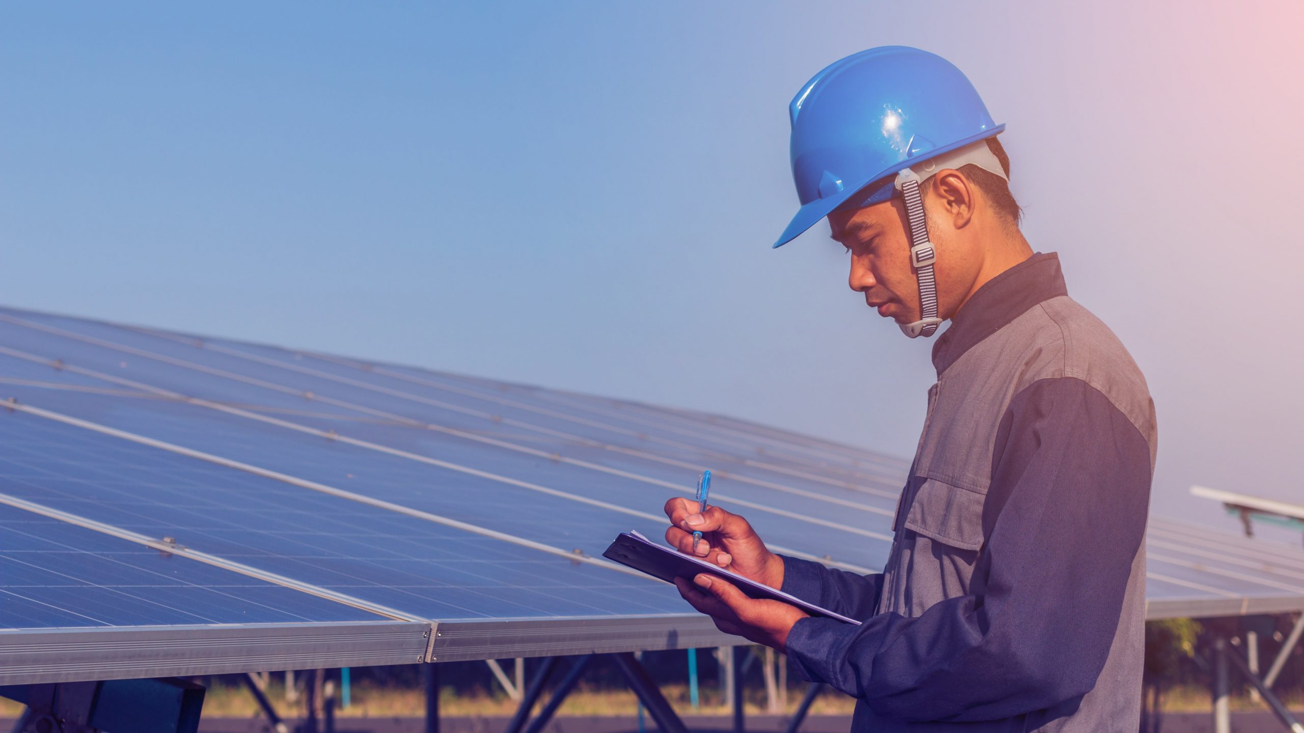 man reading from a clipboard in front of solar panels