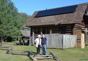 Couple with their solar-powered log cabin that is part of their retreat near the Smoky Mountains